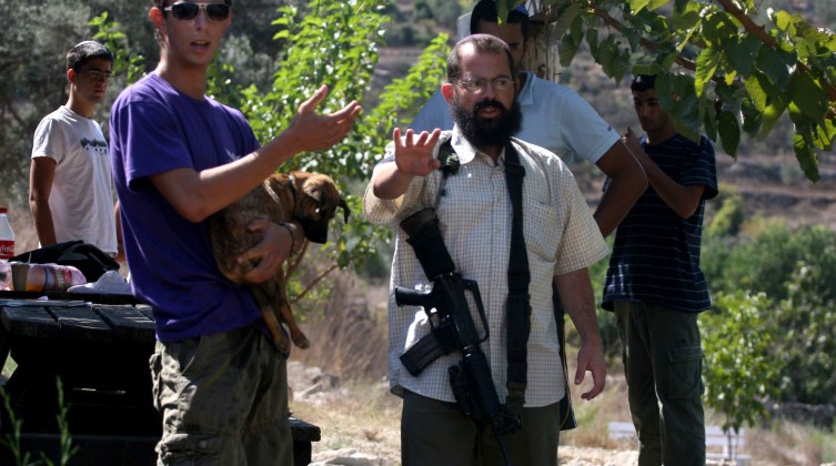 An armed Israeli settler from the Halamish settlement looks at members of pro-Palestinian volunteer-based campaign