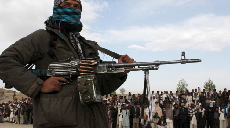 A member of the Taliban insurgent and other people stand at the site during the execution of three men in Ghazni Province