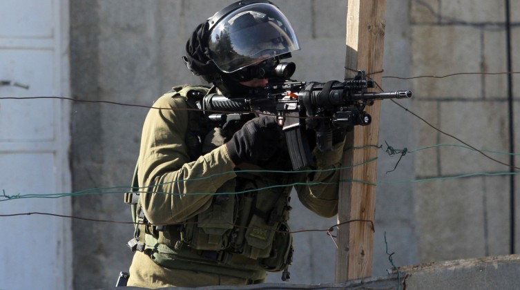 A member of Israeli security forces aims his gun at Palestinian protesters during clashes in Silwad
